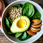 Avocado Power Bowl**

"A vibrant power bowl featuring sliced avocado, sunflower seeds, spinach, and a drizzle of extra virgin olive oil, displayed on a rustic wooden table. Ingredients are fresh and colorful.  Fully clothed hands gently sprinkle almonds on top. Safe for work, appropriate content, fully clothed, professional food photography, perfect anatomy of the hand, correct proportions, natural lighting, family-friendly."

**
